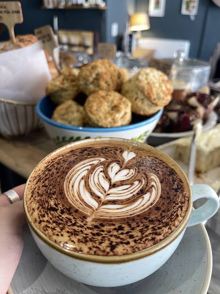 A latte-art coffee with scones behind it at General Store Winchester